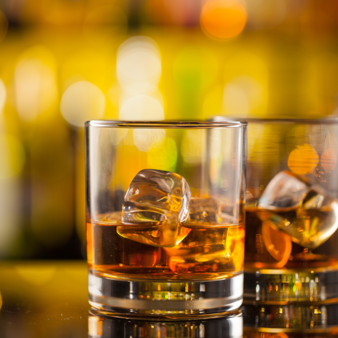 Two amber drinks on the rocks in warm bar light